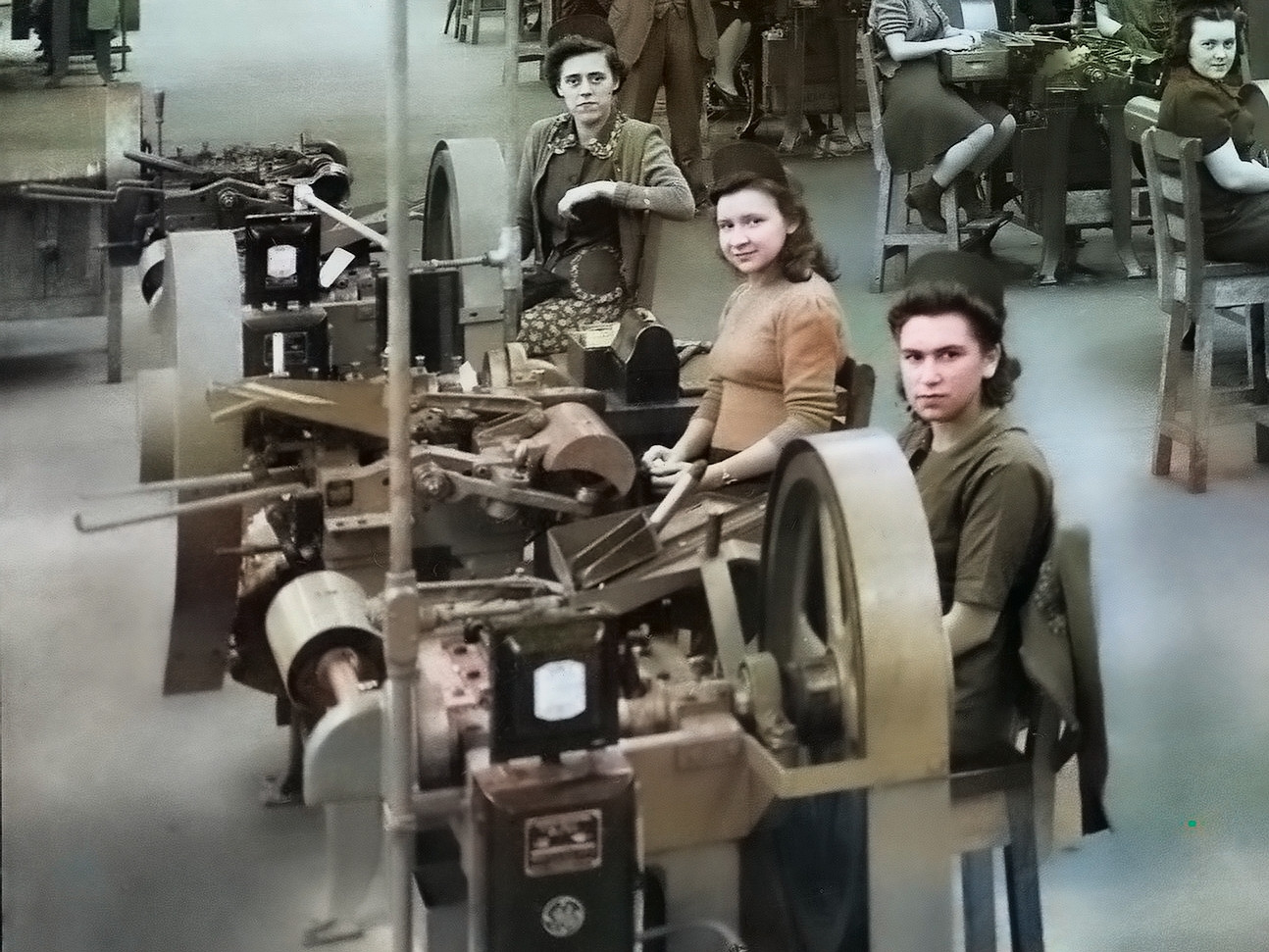 Photographie présentant des femmes derrière leur poste de travail. Chacun est relié à un système d’outillage mécanique. La Seconde Guerre mondiale force la réorganisation des installations de l’Arsenal fédéral, ancré à Québec depuis 1882. En 1939, le gouvernement décide de centraliser la fabrication des munitions de petit calibre à Québec. Les usines de Saint-Malo servent à concevoir certaines composantes des cartouches, à l’instar de l’arsenal du quartier du Palais, alors que l’assemblage s’effectue à Valcartier.